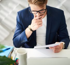 Concentrated Man Sitting At Table And Reading Documents Attentiv