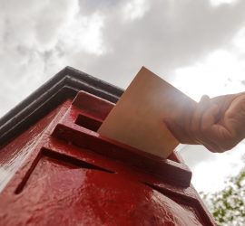 Closeup on a male hand putting a letter in a red letterbox.